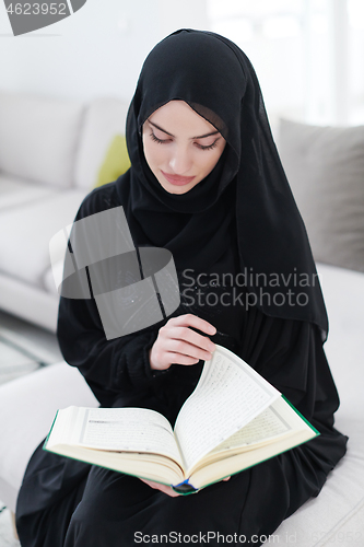 Image of young muslim woman reading Quran at home