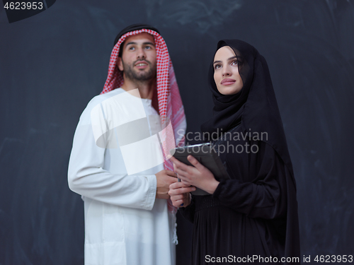 Image of muslim couple using modern technology in front of black chalkboa