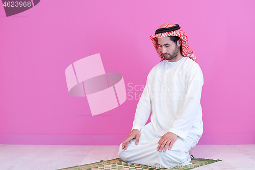 Image of young arabian muslim man praying on the floor at home