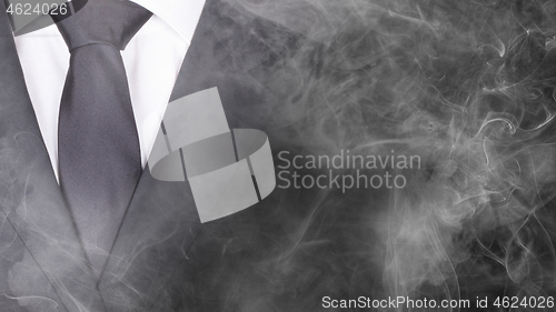 Image of Man in a black suit, standing in smoke, close-up