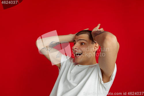 Image of Caucasian young man\'s portrait on red studio background, emotinal and expressive
