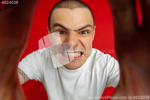 Image of Caucasian young man\'s portrait on red studio background, emotinal and expressive