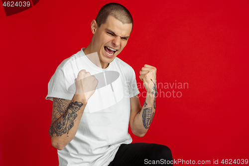 Image of Caucasian young man\'s portrait on red studio background, emotinal and expressive