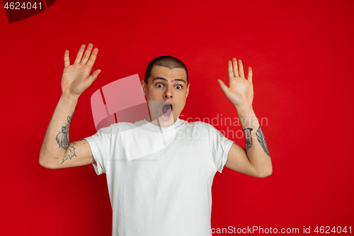 Image of Caucasian young man\'s portrait on red studio background, emotinal and expressive