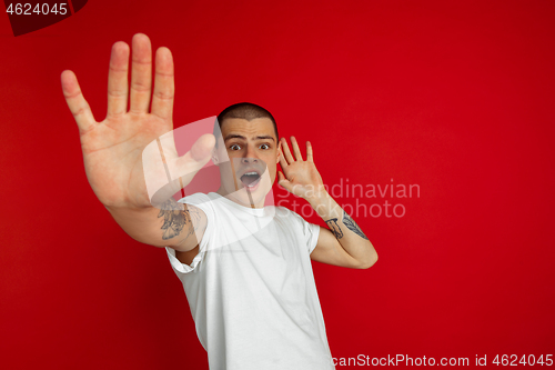 Image of Caucasian young man\'s portrait on red studio background, emotinal and expressive