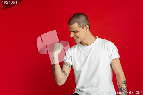 Image of Caucasian young man\'s portrait on red studio background, emotinal and expressive