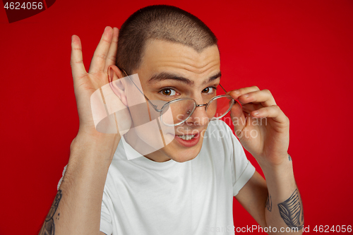 Image of Caucasian young man\'s portrait on red studio background, emotinal and expressive