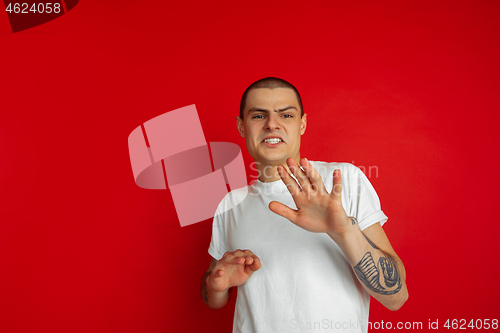 Image of Caucasian young man\'s portrait on red studio background, emotinal and expressive