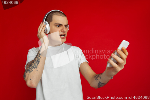 Image of Caucasian young man\'s portrait on red studio background with copyspace - emotional and expressive, angry and upset