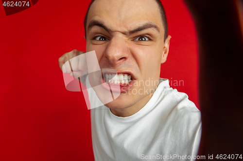 Image of Caucasian young man\'s portrait on red studio background, emotinal and expressive