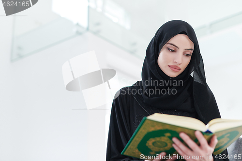 Image of young muslim woman reading Quran at home