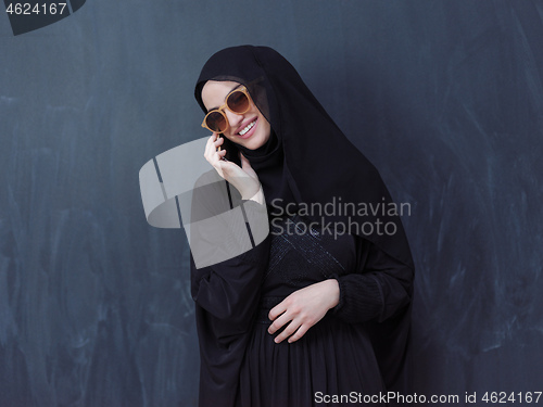 Image of young muslim woman wearing sunglasses using smartphone