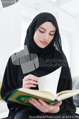 Image of young muslim woman reading Quran at home