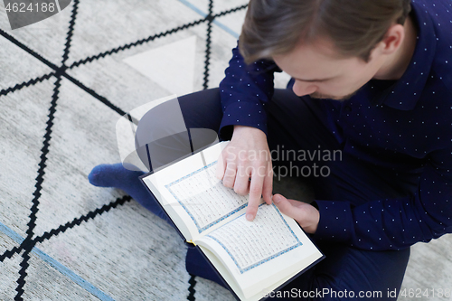 Image of young muslim man reading Quran at home