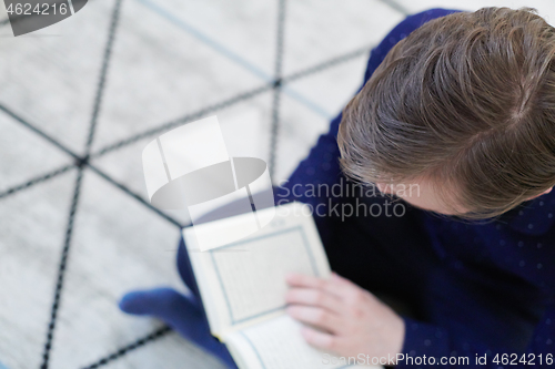 Image of young muslim man reading Quran at home