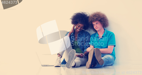 Image of multiethnic couple sitting on the floor using a laptop and table
