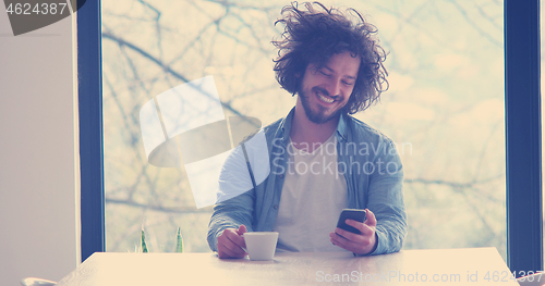 Image of young man drinking coffee and using a mobile phone  at home