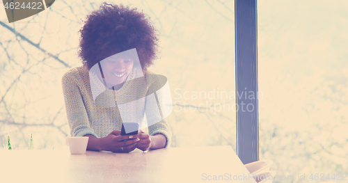 Image of black woman drinking coffee and using a mobile phone  at home