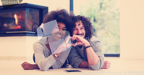 Image of multiethnic couple showing a heart with their hands on the floor