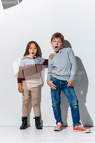 Image of The portrait of cute little boy and girl in stylish jeans clothes looking at camera at studio