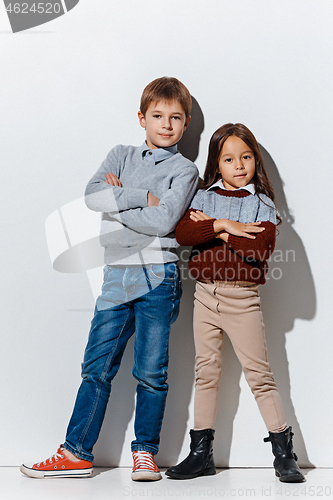 Image of The portrait of cute little boy and girl in stylish jeans clothes looking at camera at studio