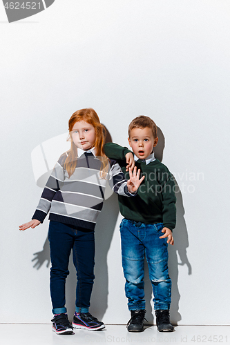 Image of The portrait of cute little boy and girl in stylish jeans clothes looking at camera at studio