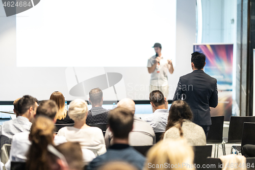 Image of Businessman in audience standing and asking question to speeker at business conference.