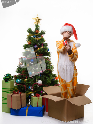 Image of A girl stands in a box, holds a New Year\'s gift and covers her face with her hand