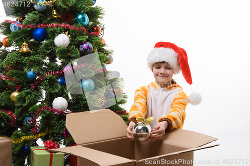 Image of A girl decorates a Christmas tree and takes out Christmas toys from a box