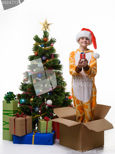 Image of Cheerful girl holds a gift in her hands and stands in a box for storing Christmas toys