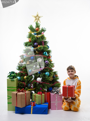 Image of A child holds a gift while sitting by the Christmas tree