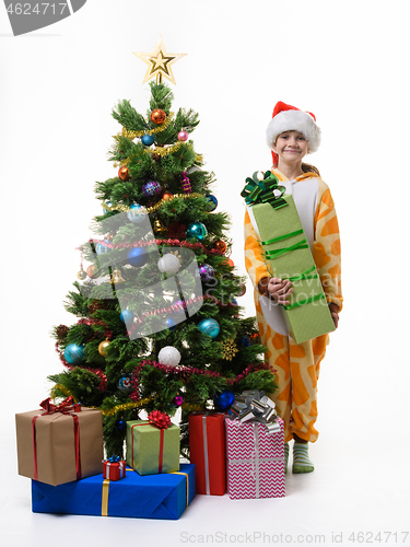 Image of A girl stands near the Christmas tree with a big New Year\'s gift