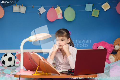 Image of Girl doing homework at home at the table by the bed