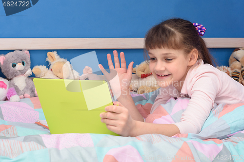 Image of A schoolgirl studies remotely at home, lies in bed and watches a video lesson