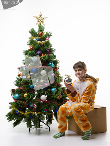 Image of A girl sits on a box for storing Christmas decorations and holds a ball in her hands