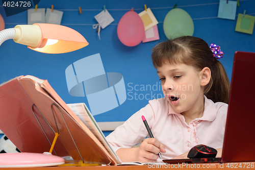 Image of The girl does lessons for a long time and yawns while sitting at the table