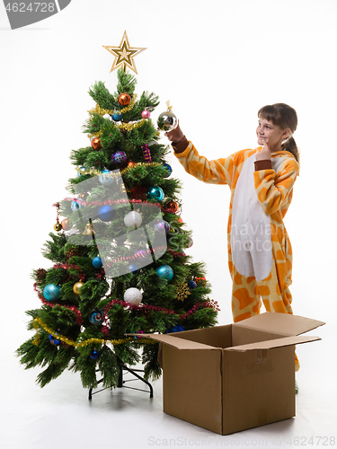 Image of A girl looks where it is better to hang a ball decorating a Christmas tree