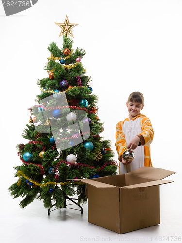 Image of Girl examines Christmas decorations pulling them out of the Christmas tree