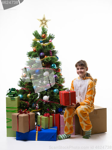 Image of Happy little girl sits by the Christmas tree and holds a New Year\'s gift