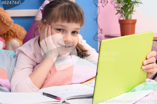 Image of Happy girl lying at home in bed and watching school video lessons