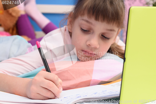 Image of The girl lies in bed and with the help of online services does her homework