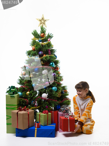 Image of Girl takes out a gift from under the Christmas tree