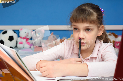 Image of The girl does homework at home and, thinking, stuck a pen in her nose