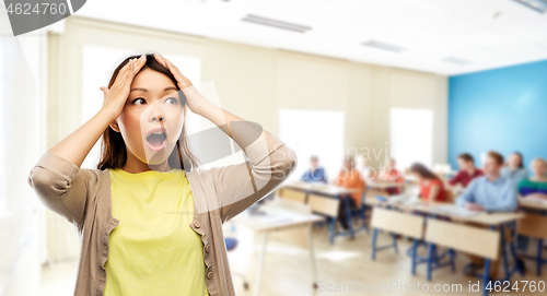 Image of stressed asian woman holding to her head at school