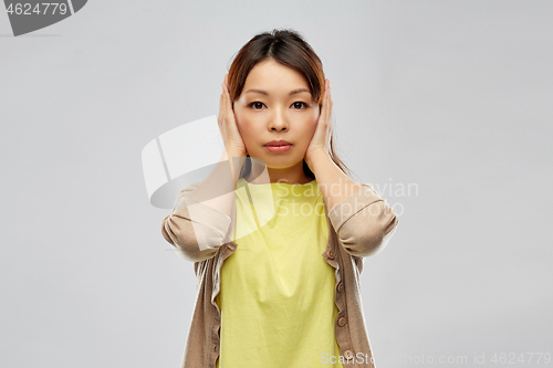 Image of asian woman closing ears by hands