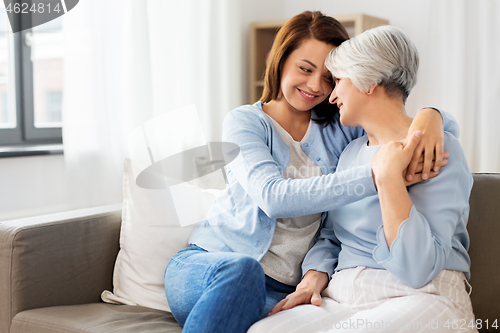 Image of senior mother with adult daughter hugging at home