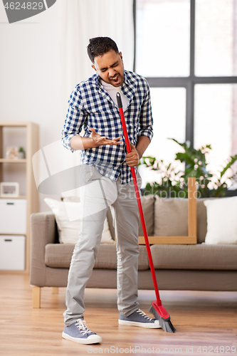 Image of man with broom cleaning and singing at home