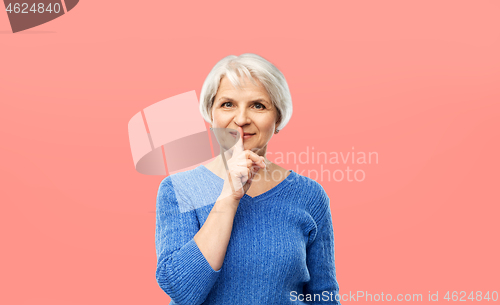 Image of senior woman making shush gesture over pink