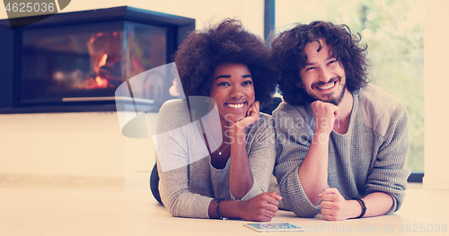 Image of multiethnic couple lying on the floor  in front of fireplace