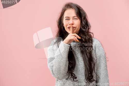 Image of The young woman whispering a secret behind her hand pink background